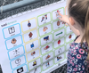 A young girl points to ‘want’ on a vinyl core vocabulary word sign featuring picture communication symbols